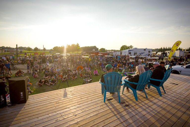 Fans watch an interview on a stage at a motocross race.